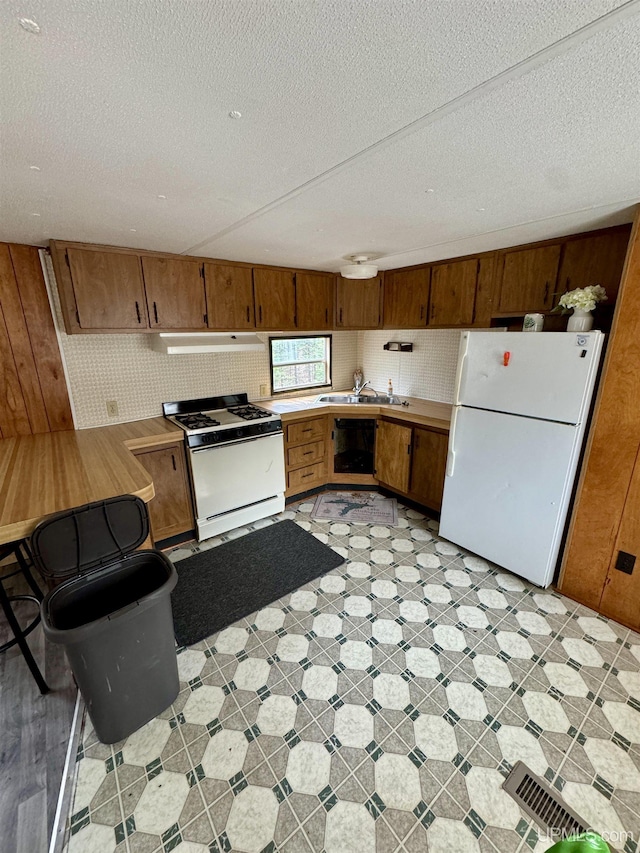 kitchen featuring white appliances, light countertops, a textured ceiling, a sink, and exhaust hood