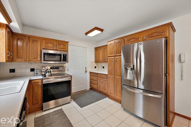 kitchen with brown cabinetry, decorative backsplash, light countertops, appliances with stainless steel finishes, and light tile patterned floors