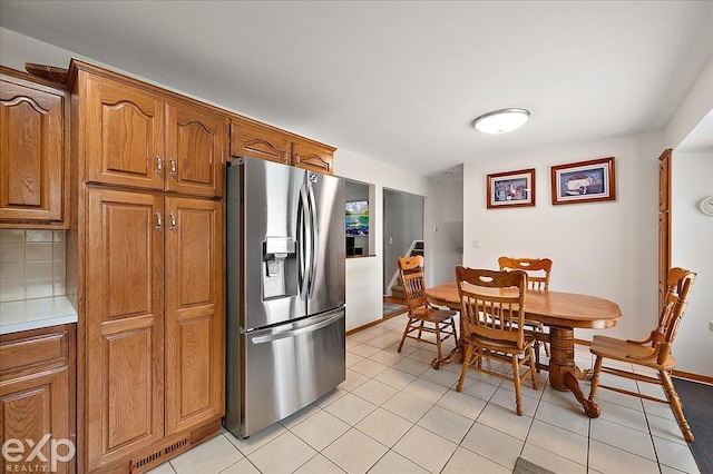 kitchen with stainless steel fridge, light countertops, brown cabinets, backsplash, and light tile patterned floors
