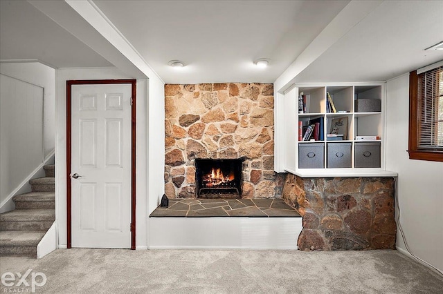 unfurnished living room with baseboards, carpet, stairs, and a stone fireplace