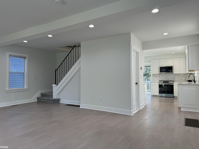 unfurnished living room with baseboards, stairs, wood finished floors, and visible vents