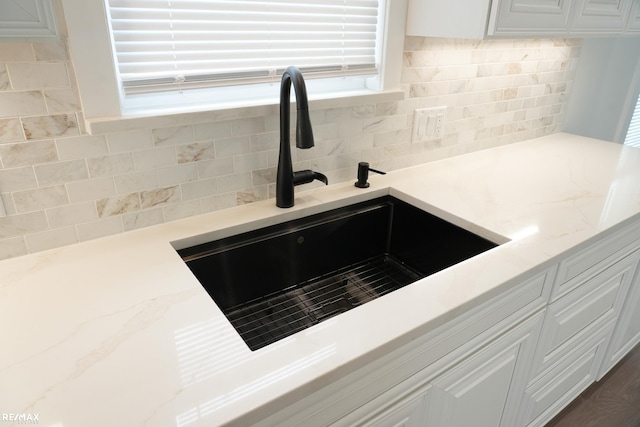 room details with backsplash, white cabinetry, light stone counters, and a sink