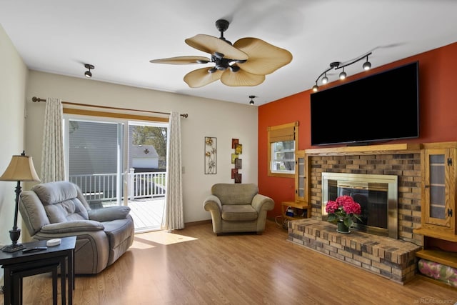 living room with a brick fireplace, a ceiling fan, and wood finished floors