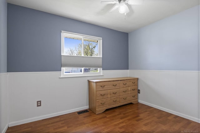 bedroom with a ceiling fan, wainscoting, wood finished floors, and visible vents