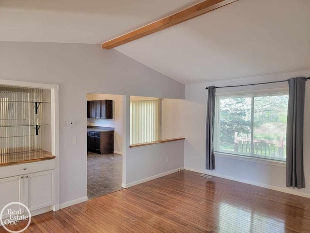 interior space featuring vaulted ceiling with beams, baseboards, visible vents, and wood finished floors