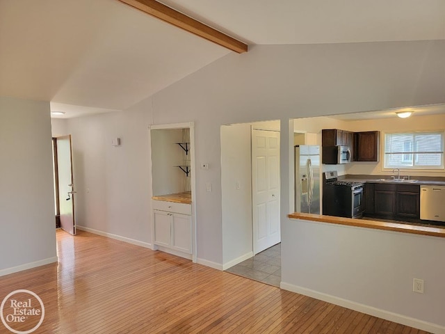 kitchen with dark brown cabinetry, lofted ceiling with beams, a sink, light wood-style flooring, and stainless steel appliances