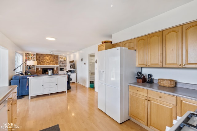 kitchen with white refrigerator with ice dispenser, a fireplace, light countertops, light wood-style flooring, and open floor plan