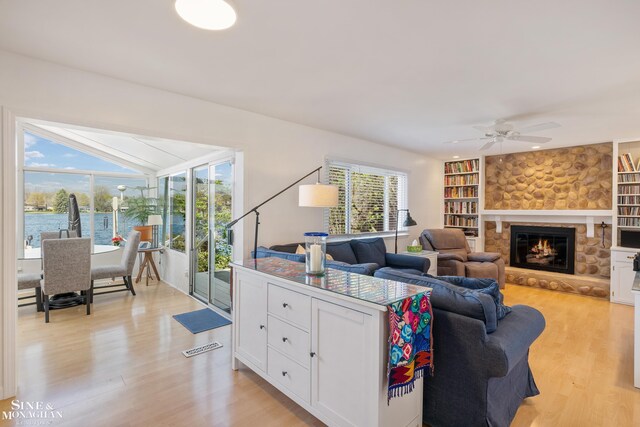 living room with ceiling fan, built in shelves, light wood-style flooring, and a fireplace