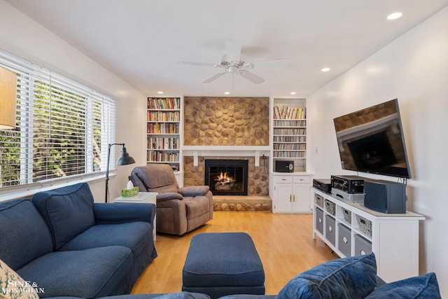 living room with built in features, a fireplace, a ceiling fan, and light wood-type flooring