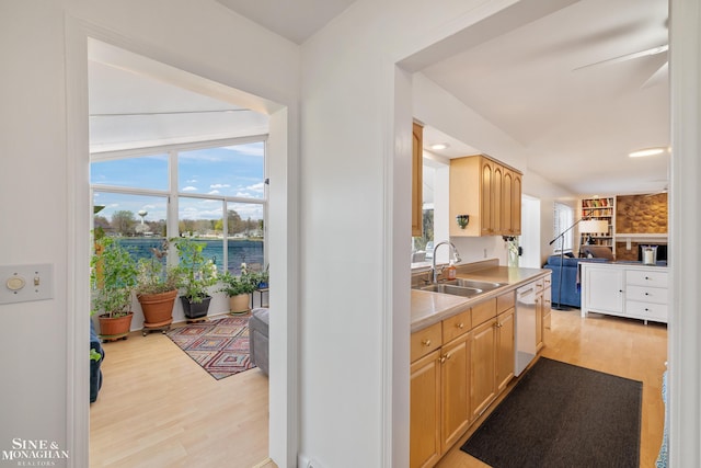 kitchen with light brown cabinetry, white dishwasher, a sink, light countertops, and light wood-type flooring