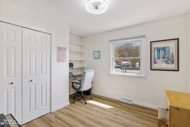 office space with baseboards, light wood finished floors, built in shelves, and visible vents