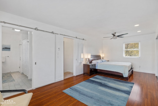 bedroom featuring a ceiling fan, a barn door, wood finished floors, baseboards, and recessed lighting