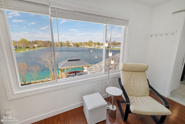 sitting room featuring baseboards, a water view, and wood finished floors