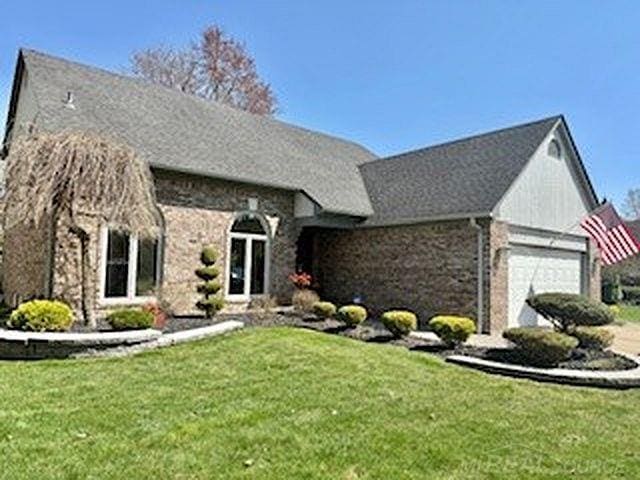 view of front facade with an attached garage, brick siding, a front lawn, and stone siding