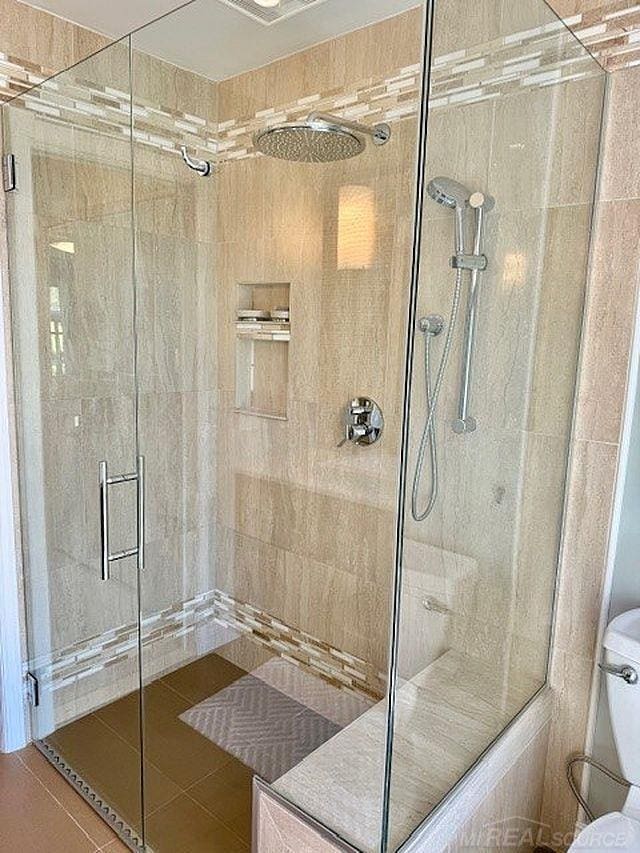 bathroom featuring toilet, tile patterned floors, and a shower stall