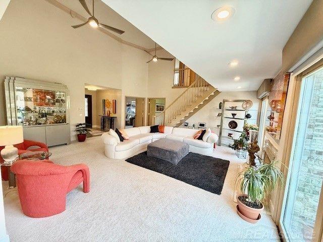 living area with carpet floors, a ceiling fan, a high ceiling, and stairway