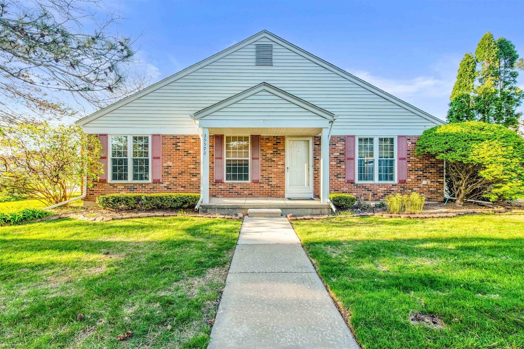 view of front of home featuring brick siding, a front lawn, and covered porch