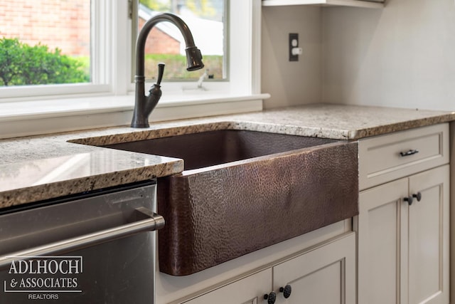 interior details featuring stainless steel dishwasher, white cabinetry, light stone countertops, and a sink