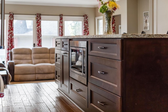 interior space with stainless steel microwave, dark wood-style flooring, light stone countertops, and dark brown cabinetry