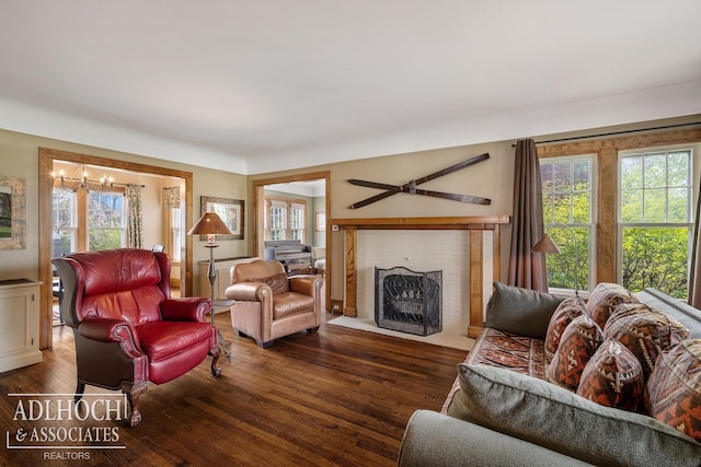 living area with a brick fireplace, a notable chandelier, wood finished floors, and a wealth of natural light