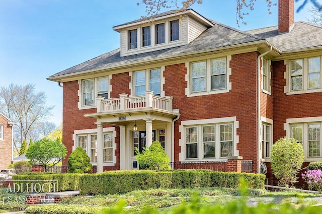 view of front of home with brick siding, a shingled roof, a balcony, and a chimney