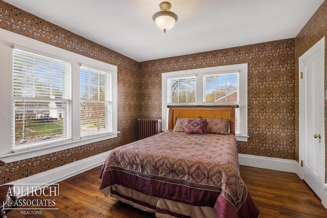bedroom featuring radiator heating unit, baseboards, wallpapered walls, and wood finished floors
