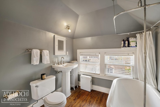 bathroom featuring a healthy amount of sunlight, vaulted ceiling, wood finished floors, toilet, and a soaking tub