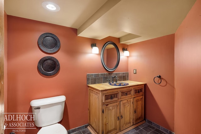half bath with vanity, tile patterned flooring, toilet, baseboards, and backsplash