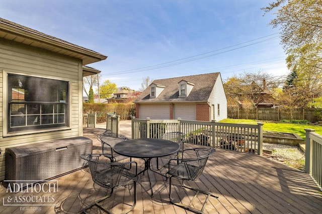 wooden deck featuring outdoor dining area, a lawn, an outbuilding, a garage, and a fenced backyard