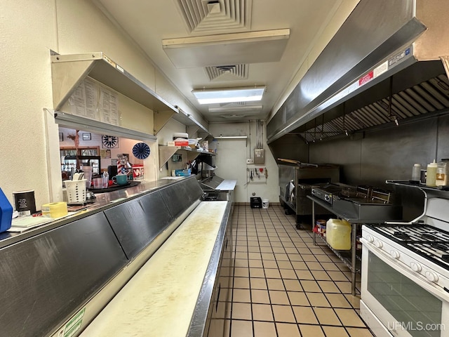 interior space featuring visible vents, white range with gas stovetop, light countertops, wall chimney exhaust hood, and light tile patterned floors