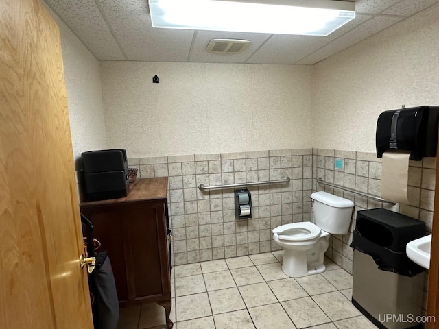 bathroom featuring tile walls, toilet, visible vents, and a drop ceiling