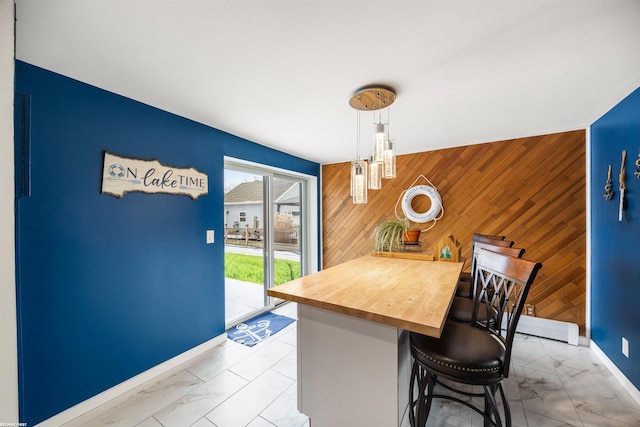 kitchen featuring a breakfast bar, wood walls, marble finish floor, an accent wall, and baseboards