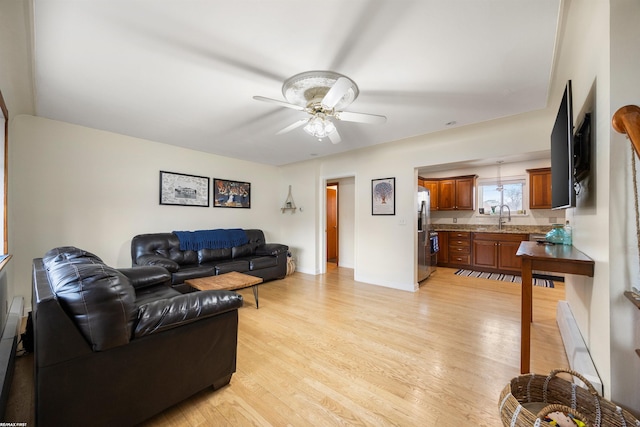 living area featuring light wood-style floors, baseboards, and ceiling fan