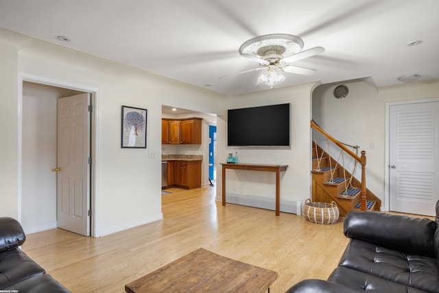 living area featuring stairway, ceiling fan, baseboards, and light wood finished floors