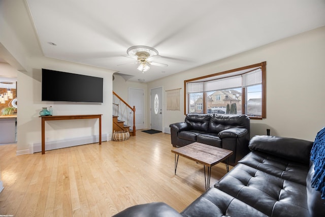 living room featuring stairs, a ceiling fan, baseboards, and light wood-type flooring