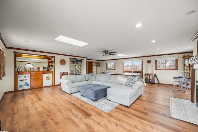 living area with crown molding, light wood-style floors, a ceiling fan, baseboards, and indoor bar