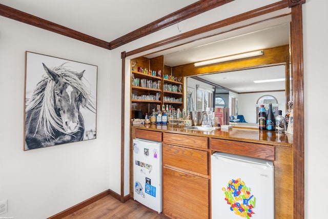 bar featuring ornamental molding, fridge, light wood-style floors, a sink, and wet bar