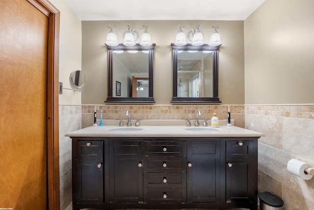 full bath with double vanity, tile walls, a sink, and a wainscoted wall