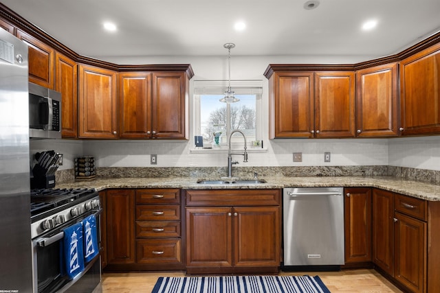 kitchen with light stone countertops, hanging light fixtures, a sink, light wood-style floors, and stainless steel appliances