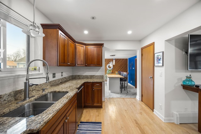 kitchen with a sink, light wood-style flooring, stone counters, and decorative light fixtures