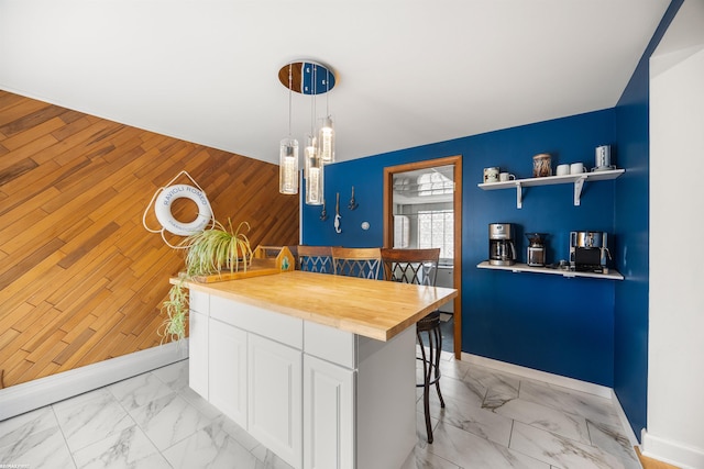kitchen featuring a kitchen breakfast bar, wooden counters, marble finish floor, white cabinetry, and pendant lighting