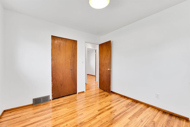 unfurnished bedroom with baseboards, visible vents, wood finished floors, and a closet