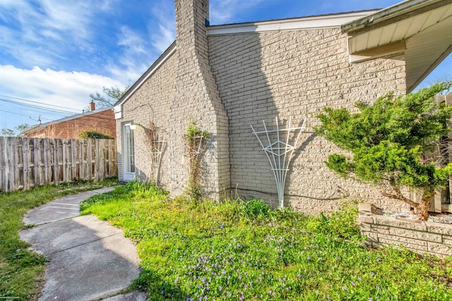 view of home's exterior featuring fence, a chimney, and brick siding
