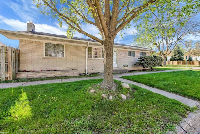 view of front of home featuring fence, a chimney, a front lawn, and brick siding