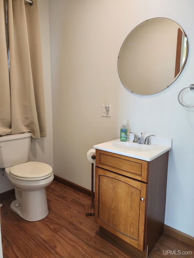 half bathroom featuring toilet, baseboards, wood finished floors, and vanity