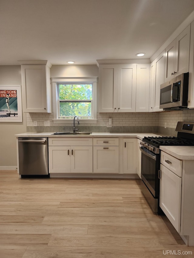 kitchen featuring decorative backsplash, light countertops, white cabinets, a sink, and stainless steel appliances