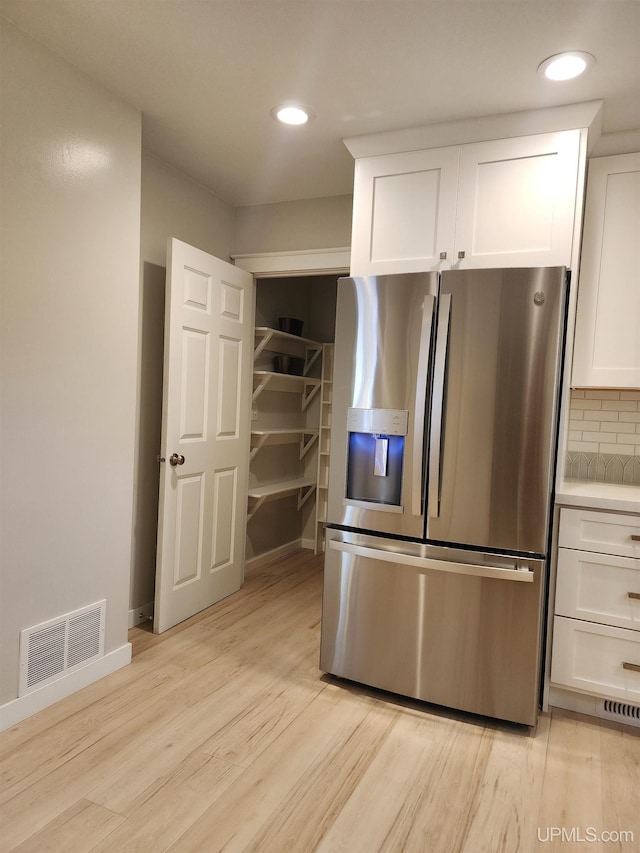 kitchen featuring visible vents, stainless steel fridge with ice dispenser, light wood-type flooring, white cabinets, and tasteful backsplash