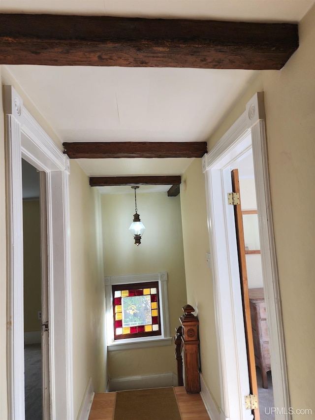 hall featuring baseboards, beam ceiling, and wood finished floors