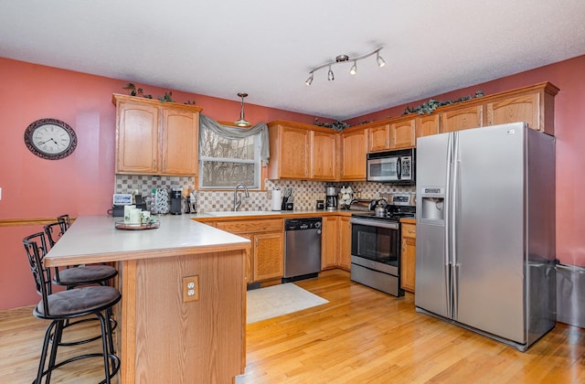 kitchen with stainless steel appliances, a sink, light wood finished floors, and a peninsula