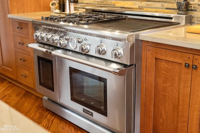 room details featuring light countertops, brown cabinetry, backsplash, and range with two ovens